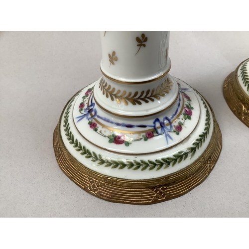 20 - A pair of French porcelain and gilt metal mounted candlesticks, hand painted with ribboned swags of ... 