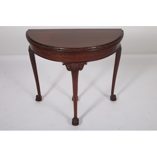 33 - A GEORGIAN DESIGN MAHOGANY FOLD OVER CARD TABLE of demilune outline the shaped top with carved rim a... 