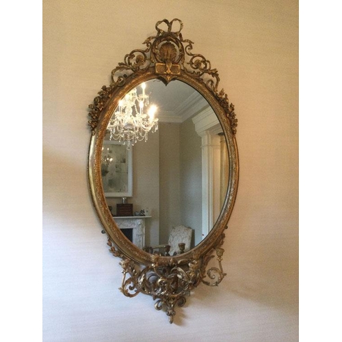 67 - A 19TH CENTURY GILTWOOD AND GESSO MIRROR the oval plate within a foliate moulded frame with shell C-... 