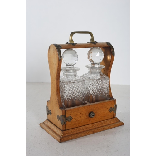 606 - A VINTAGE OAK AND BRASS BOUND TWO BOTTLE TANTALUS with cut glass decanters and stoppers 32cm (h) x 2... 