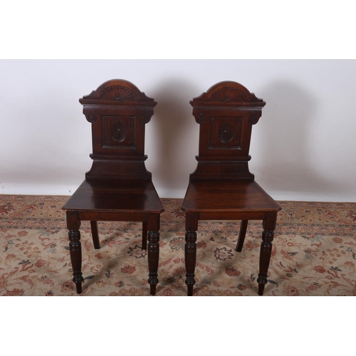 93 - A PAIR OF VINTAGE MAHOGANY HALL CHAIRS each with a carved back and panelled seat on turned legs