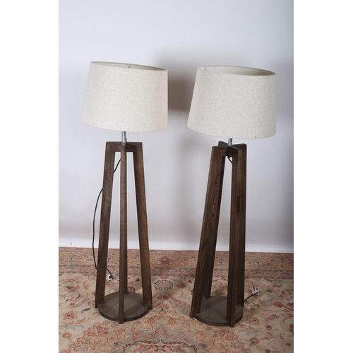 94 - A PAIR OF CONTEMPORARY STAINED WOOD FLOOR STANDARD LAMPS each raised on moulded supports above a cir... 