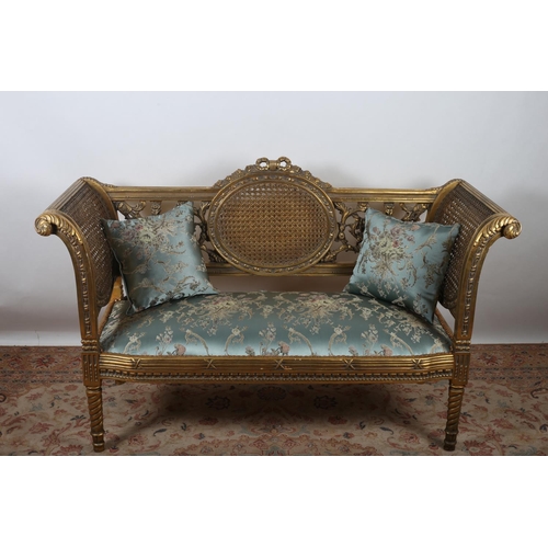 48 - A FRENCH GILT FRAMED UPHOLSTERED AND CANED SETTEE with ribbon tied and flower head cresting above an... 