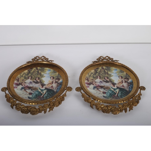 838 - A PAIR OF CONTINENTAL BRASS AND PORCELAIN WALL PLACQUES EACH OF CIRCULAR OUTLINE decorated with fema... 