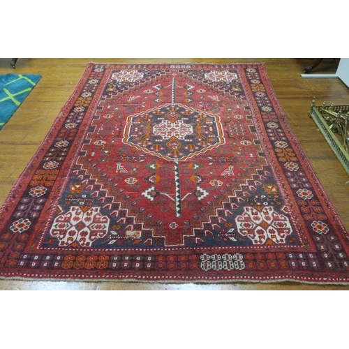 121 - AN ORIENTAL WOOL RUG the wine indigo and beige ground with central panel filled with palmets, hooks ... 