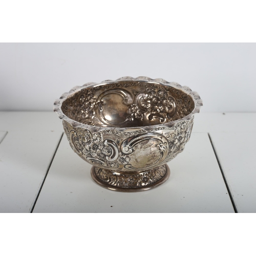 395 - A SILVER EMBOSSED BOWL decorated with flowerheads and C-scrolls raised on a circular spreading foot ... 