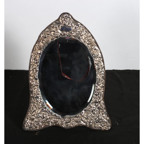 242 - A SILVER EMBOSSED DRESSING TABLE MIRROR the oval bevelled glass plate within a C-scroll decorated fr... 