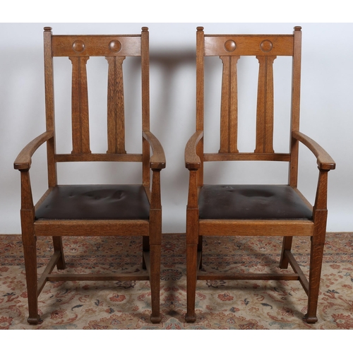 556 - A PAIR OF ARTS AND CRAFTS OAK ARMCHAIRS each with a curved top rail on vertical splats with upholste... 