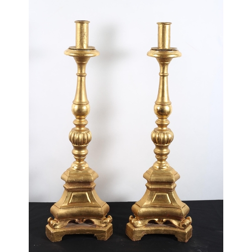 564 - A PAIR OF CONTINENTAL GILTWOOD CANDLESTICKS each with a baluster lobed column above a triform base w... 