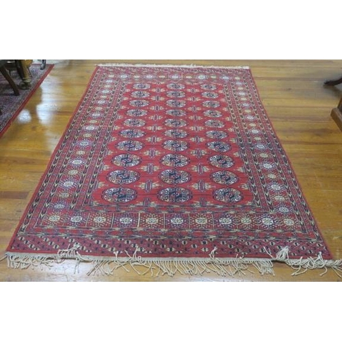 847 - A PAKISTANI BOKHARA WOOL RUG the wine ground with central panel filled with rosettes within a confor... 