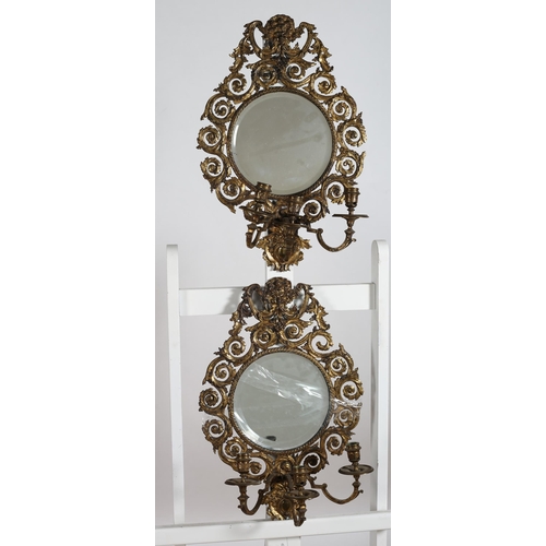 111 - A PAIR OF BRASS GIRANDOLE MIRRORS each with a circular bevelled glass plate within a pierced C-scrol... 