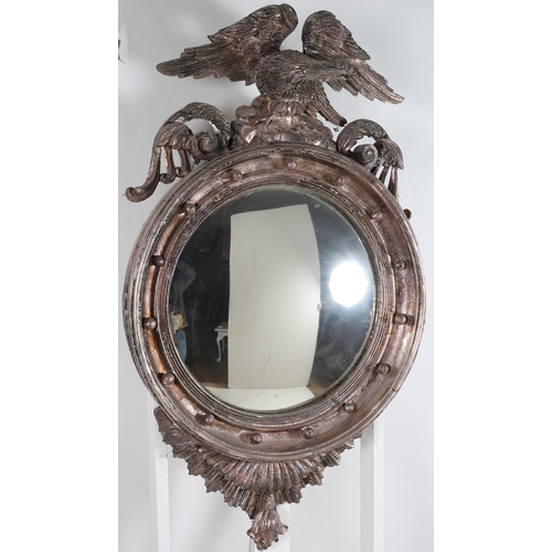 742 - A SILVERED CONVEX MIRROR the ball decorated frame surmounted by a winged eagle perched on a rockwork... 