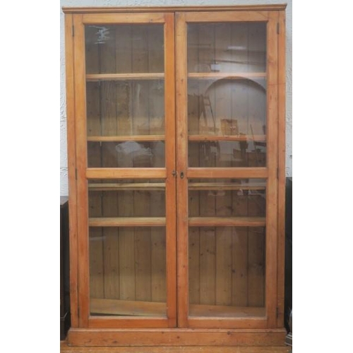 8 - A VINTAGE PINE TWO DOOR BOOKCASE the moulded cornice above a pair of glazed doors containing adjusta... 
