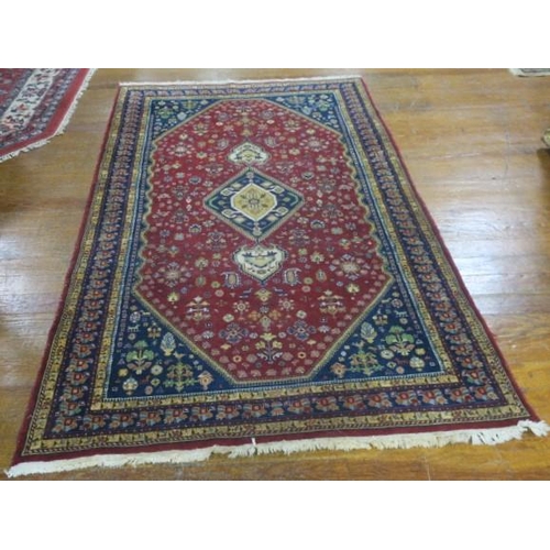 550 - A KERMAN WOOL RUG the wine and indigo ground with central panel filled with stylised flowerheads and... 