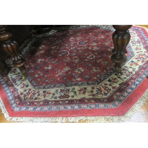 553 - AN ORIENTAL WOOL RUG of octagonal outline the wine ground with central floral panel within a conform... 