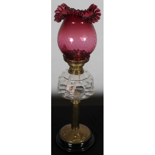 565 - A VINTAGE BRASS RUBY GLASS AND CLEAR GLASS OIL LAMP the engraved reservoir above a cylindrical colum... 