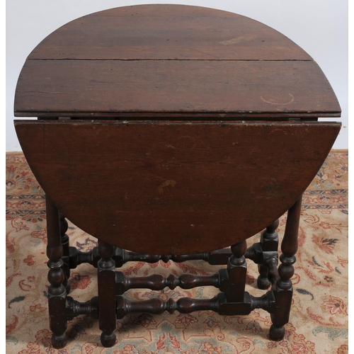 79 - AN EARLY OAK DROP LEAF TABLE the oval hinged top raised on baluster supports with bun feet joined by... 