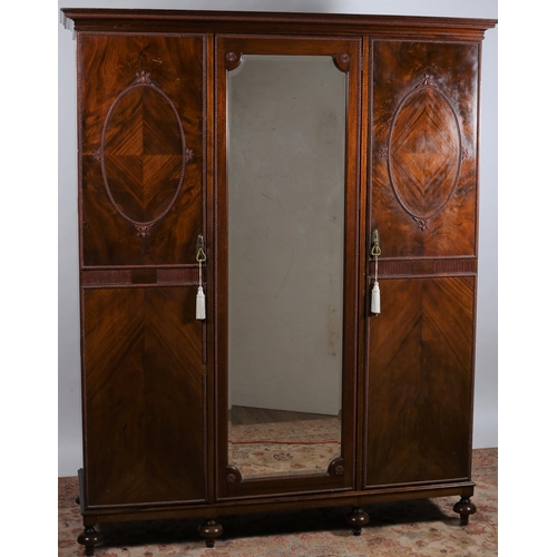 4 - A VINTAGE MAHOGANY THREE DOOR WARDROBE the moulded cornice above a bevelled glass mirrored door flan... 