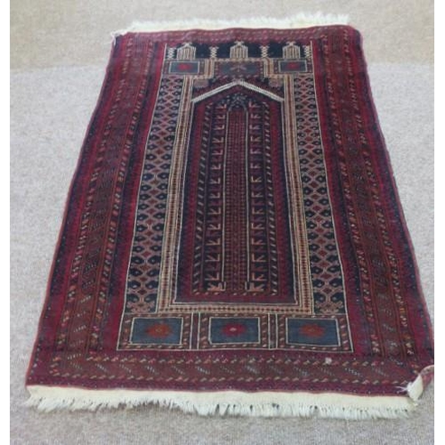 549 - AN ORIENTAL PRAYER RUG the indigo and wine ground with central panel filled with serrated hooks and ... 