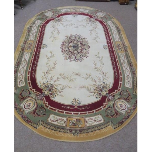 560 - A BEIGE WINE AND LIGHT GREEN GROUND RUG of oval outline the central panel filled with flowerheads an... 