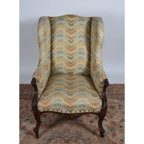 224 - AN EDWARDIAN CARVED MAHOGANY UPHOLSTERED WING CHAIR with foliate carved arm supports on cabriole leg... 