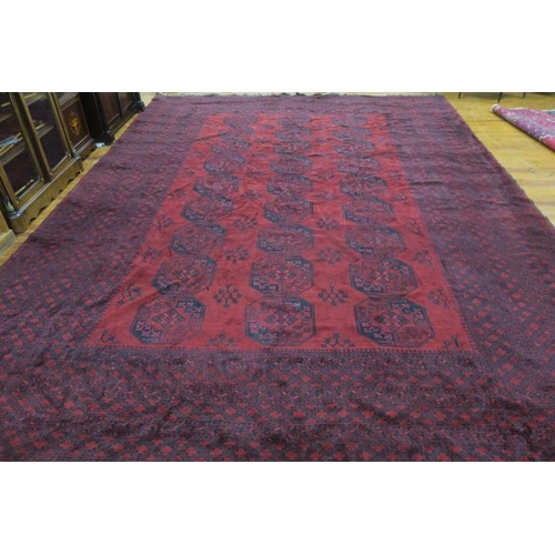 359 - AN ORIENTAL WOOL RUG the wine ground with a central panel filled with serrated panel, stylised flowe... 