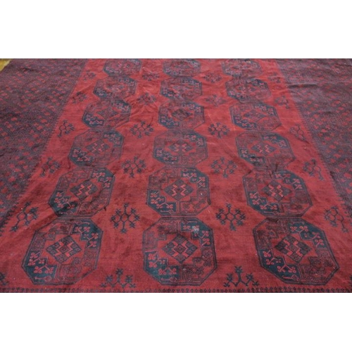 359 - AN ORIENTAL WOOL RUG the wine ground with a central panel filled with serrated panel, stylised flowe... 