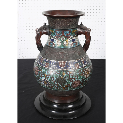 557 - A BRONZE AND CLOISONNE VASE of bulbous outline with figural mask handles raised on a hardwood stand ... 