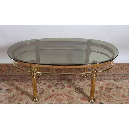 206 - A GILT BRASS AND GLAZED COFFEE TABLE of oval outline the shaped top raised on cylindrical supports j... 