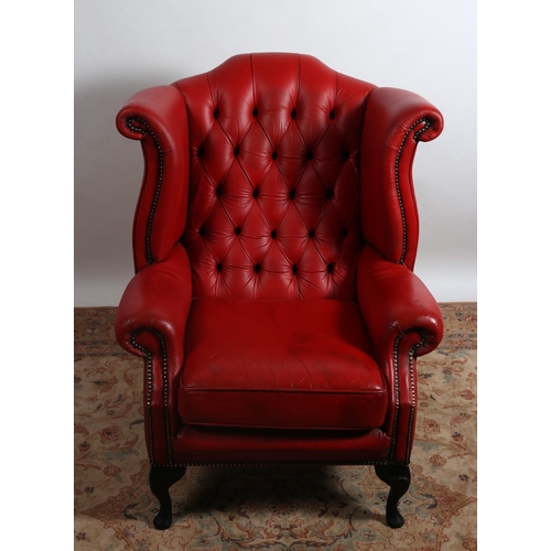 342 - A RED HIDE UPHOLSTERED WINGED LIBRARY ARMCHAIR with deep buttoned upholstered back scroll over arms ... 