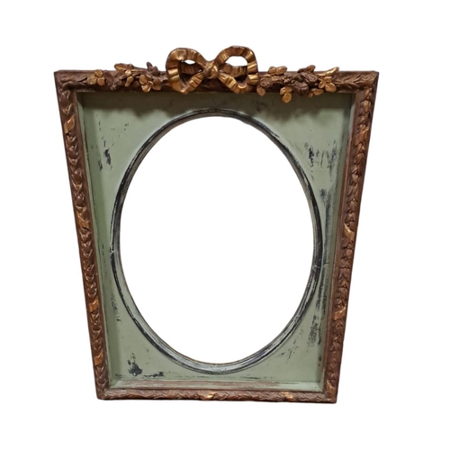 673 - A GILTWOOD AND GESSO AND POLYCHROME MIRROR the oval plate within a moulded frame with ribbon tied an... 