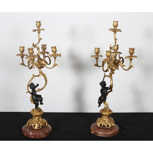 408 - A PAIR OF CONTINENTAL GILT BRASS AND BRONZE FIGURAL FIVE BRANCH CANDELABRA with foliate scroll arms ... 