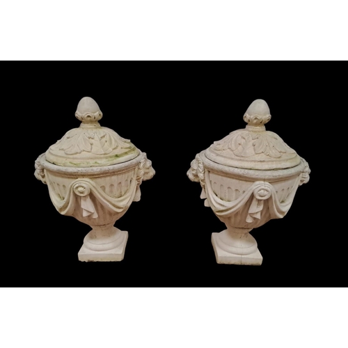 223 - A PAIR OF COMPOSITION STONE LIDDED URNS with foliate decoration above a fluted frieze hung with drap... 