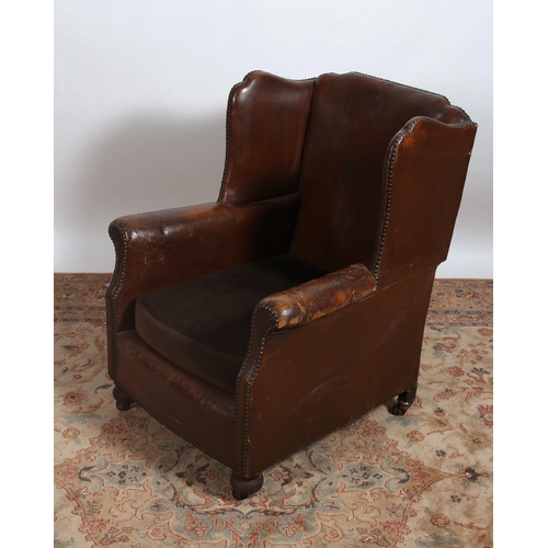 264 - A VINTAGE HIDE UPHOLSTERED WING CHAIR with scroll over arms and loose cushion on bun feet with casto... 