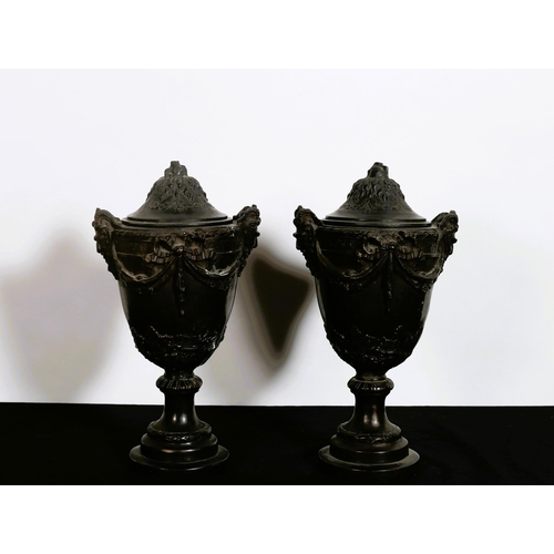 321 - A PAIR OF BRONZE LIDDED URNS each of ovoid tapering form with figural mask handles hung with ribbon ... 