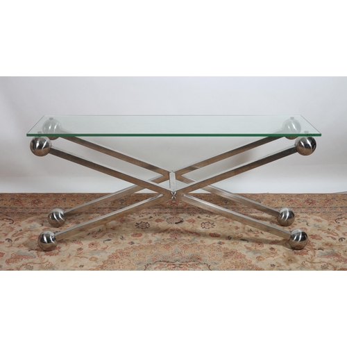 445 - A DESIGNER CHROME AND GLAZED CONSOLE TABLE of rectangular outline the shaped glazed top raised on X-... 