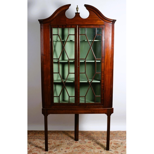 65 - A GEORGIAN MAHOGANY CORNER CABINET ON STAND the architectural pediment centred by a brass urn above ... 