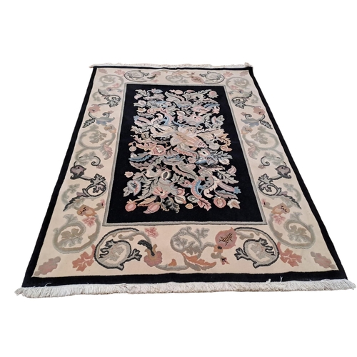 161 - A BEIGE AND JET GROUND PATTERN RUG the central panel filled with flowerheads and foliage within a co... 