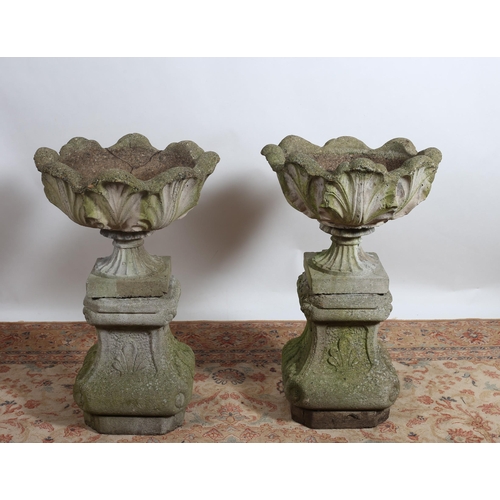 206 - A PAIR OF COMPOSITION STONE URNS the leaf shaped bowls above a spreading sockle on platform base and... 