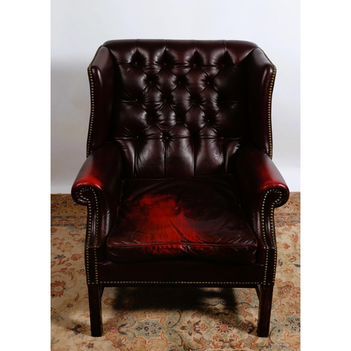 231 - A GEORGIAN STYLE HIDE UPHOLSTERED AND MAHOGANY WING BACK LIBRARY CHAIR with deep buttoned upholstere... 