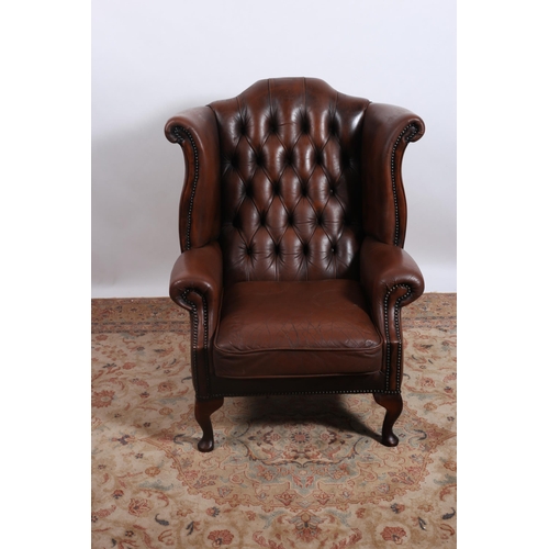 335 - A VINTAGE HIDE UPHOLSTERED WINGED CHAIR with deep buttoned upholstered back and scroll over arms wit... 