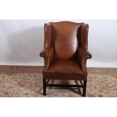 346 - A VINTAGE MAHOGANY AND HIDE UPHOLSTERED WINGED CHAIR with scroll over arms and brass studding on squ... 