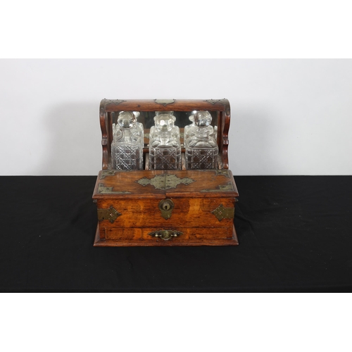 410 - A VINTAGE OAK AND PLATED BOUND TANTALUS with hinged compartment containing cut glass decanters with ... 