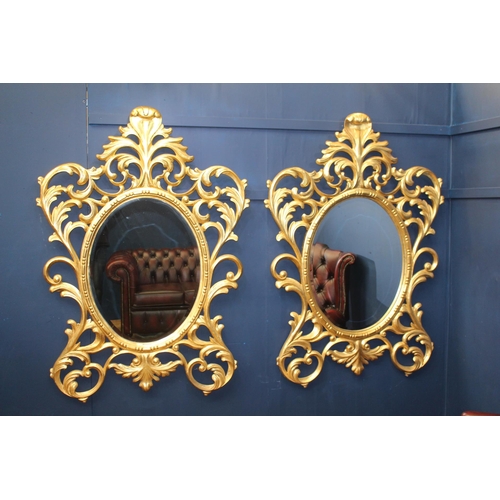 386 - A PAIR OF CONTINENTAL GILTWOOD MIRRORS the oval plate within a pierced C-scroll and foliate frame wi... 