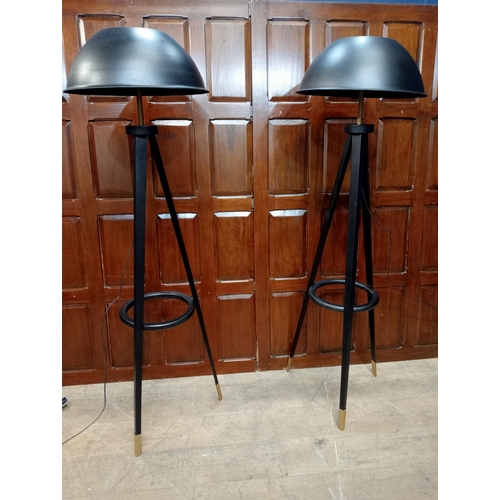 353 - A PAIR OF EBONISED AND BRASS FLOOR STANDARD LAMPS each of tripod outline with domed shaped shades on... 