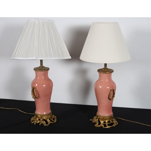 432 - A PAIR OF CHINESE CORAL GLAZED CHINA AND GILT BRASS TABLE LAMPS each of urn form the light pink grou... 