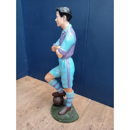 385 - A COMPOSITION AND POLYCHROME FIGURE modelled as a soccer player shown standing with arms folded on a... 