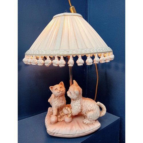 448 - A PINK AND WHITE CERAMIC TABLE LAMP modelled as two cats playing on a cushion with pleated shade 50c... 