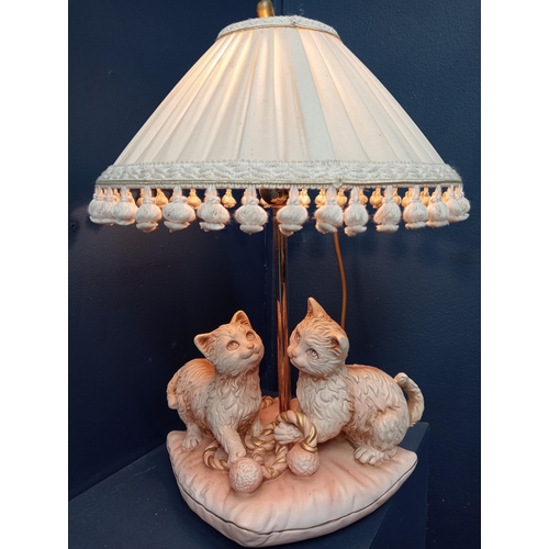 448 - A PINK AND WHITE CERAMIC TABLE LAMP modelled as two cats playing on a cushion with pleated shade 50c... 