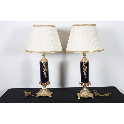 570 - A PAIR OF CONTINENTAL BLUE GLAZED AND BRASS TABLE LAMPS each with a cylindrical column hung with rib... 